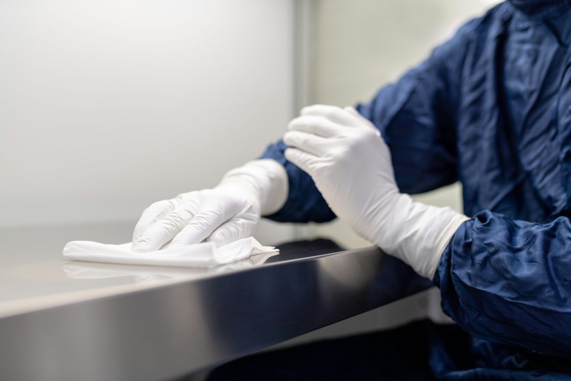 A person in a blue gown and white gloves wiping a metal surface
